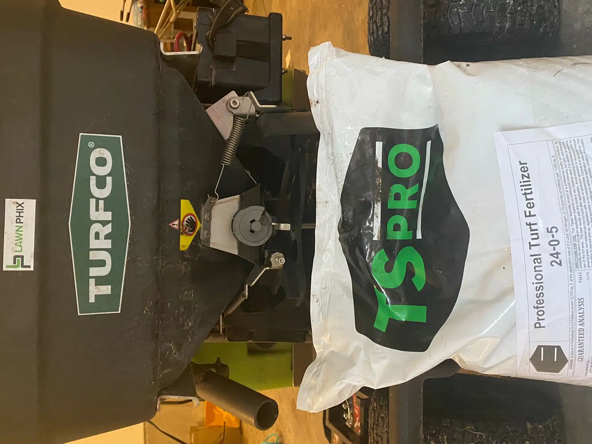 Bag of 24-0-5 fall lawn fertilizer next to a spreader